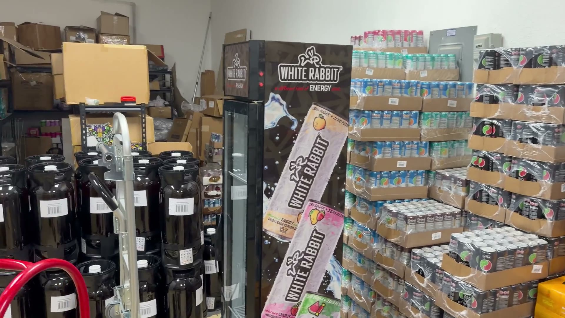 Inside the Infinity Distro stockroom: shelving and boxed stock, with cases of canned drinks and kratom seltzer stacked on pallets