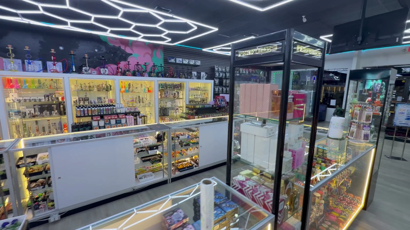 The front counter: lit wall cases with hookahs along the top and a glass counter under hexagon lights