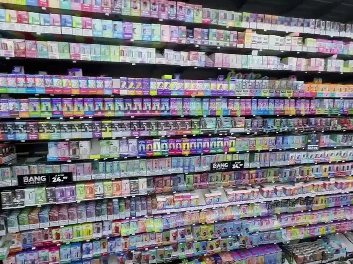 Floor-to-ceiling wall of colourful boxed vape products on black shelving