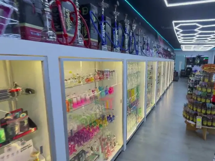 Row of lit glass display cases with colourful glass pipes inside and hookahs along the top