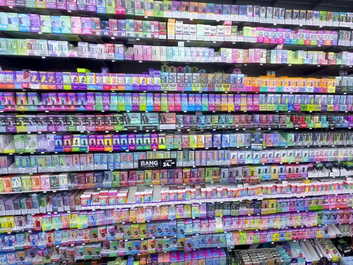 Floor-to-ceiling wall of multicoloured boxed vape products on black shelving