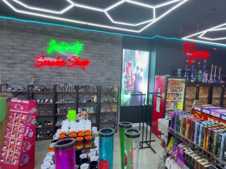 Infinity Smoke Shop neon sign on a stone wall beside cigar cabinets and an incense display