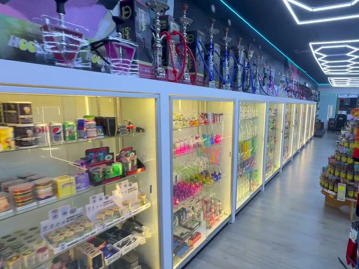 Long row of lit glass display cases with colourful glass pieces inside and hookahs along the top