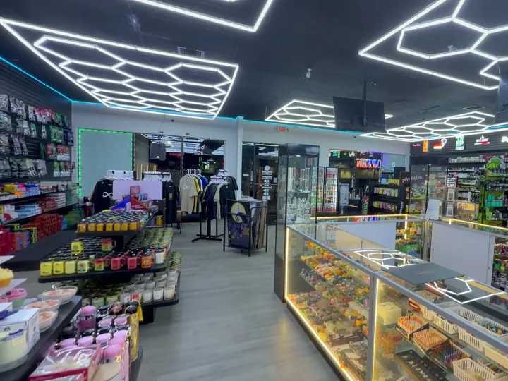 Wide view of the shop floor with a tobacco wall, candle table, clothing racks and a long glass counter