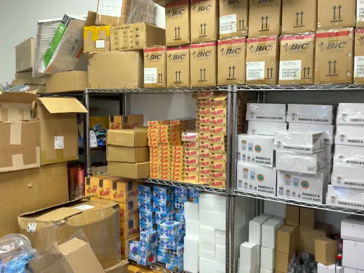 Stockroom shelves stacked with lighter cases, rolling paper boxes and boxed glass storage jars