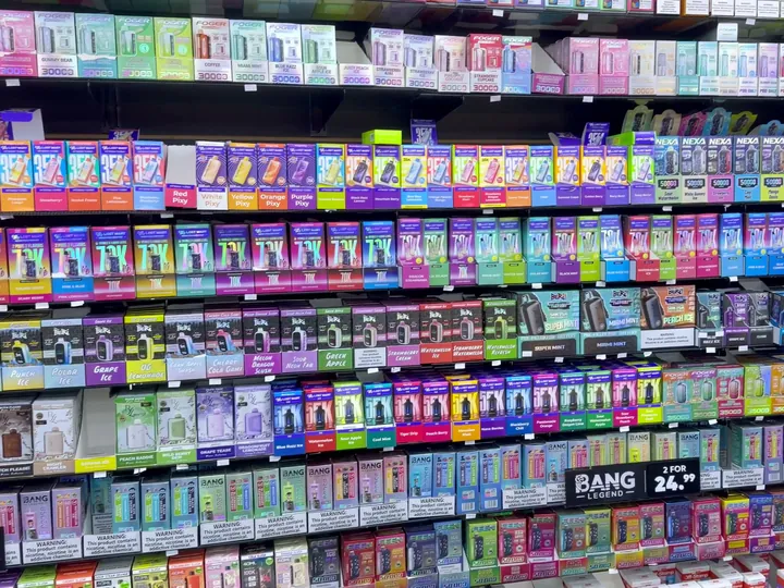 Floor-to-ceiling wall of colourful boxed disposable vapes lined up on black shelves