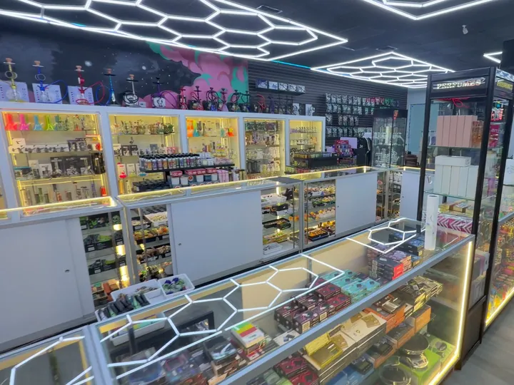 Lit white display cases under hexagon ceiling lights, with hookahs lined along the top